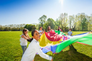 Happy boy waving colorful parachute with friends
