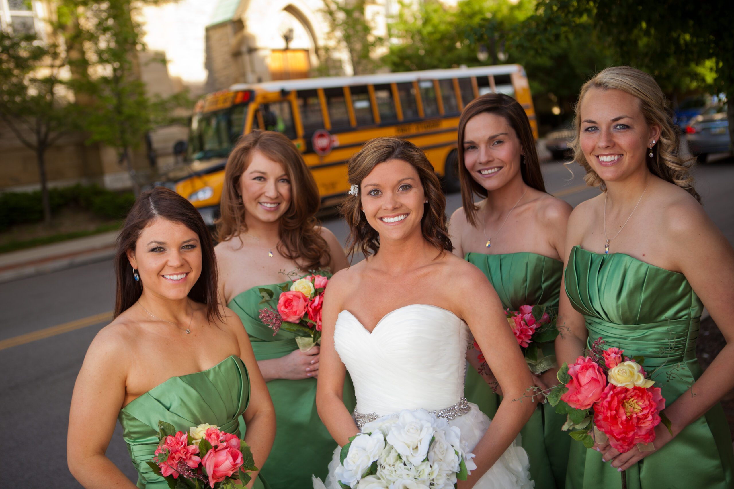 A bride and her bridesmaids standing in front of a yellow school bus, which she rented for her wedding.